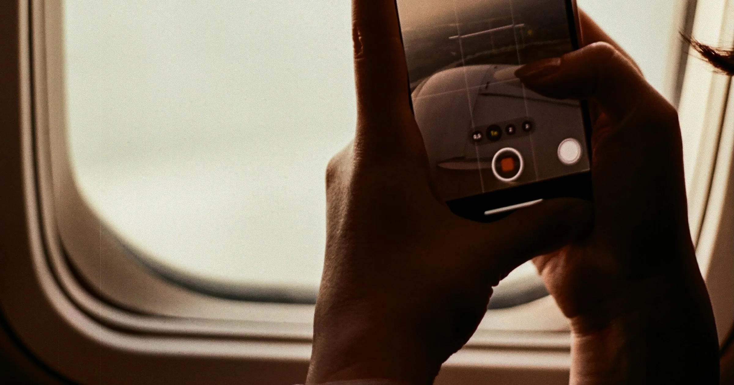 A traveller holds a phone up to an airplane window before landing