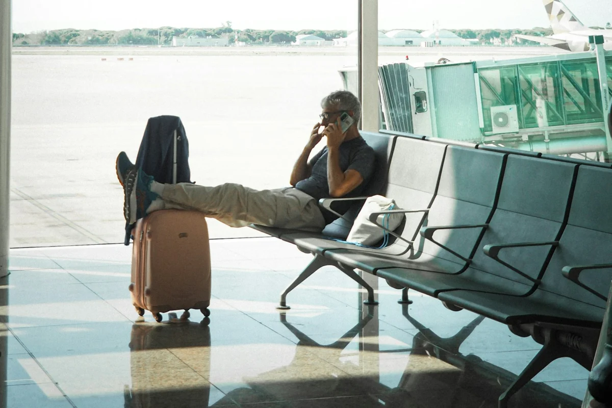 Traveller talking on a phone beside luggage in an airport waiting area