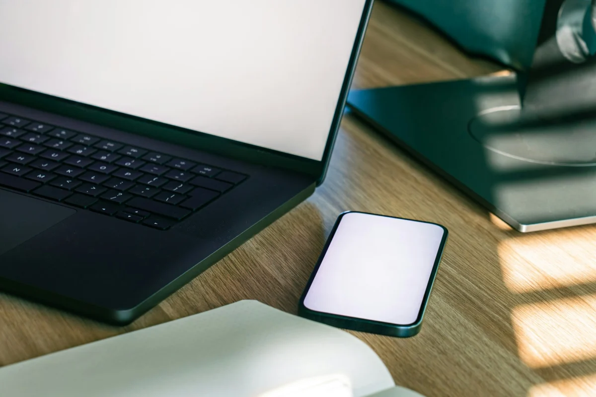 Smartphone beside an open laptop on a wooden desk.