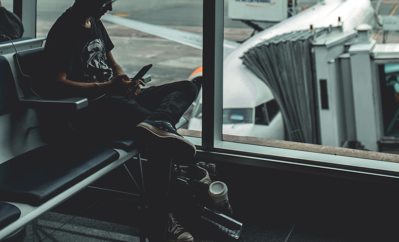 Traveller checking a smartphone beside an airport window overlooking aircraft